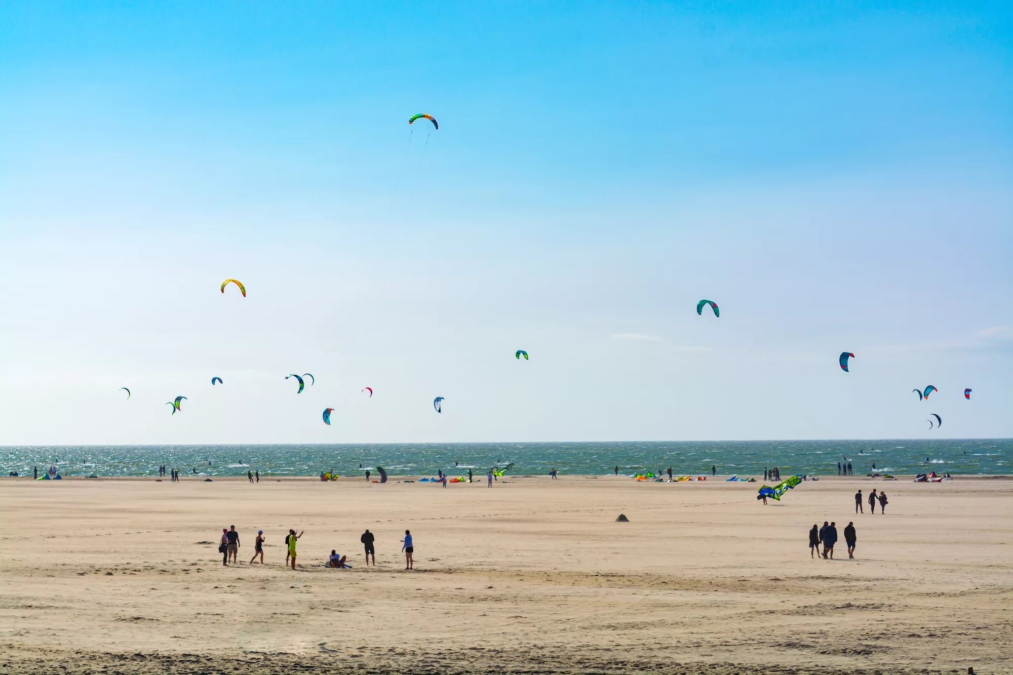 strand met mensen, en de zee met kitesurfers op de achtergrond